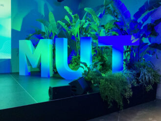 diesige 3D Buchstaben "Mut" stehen auf einer Bühne und sind blau Grün beleuchtet